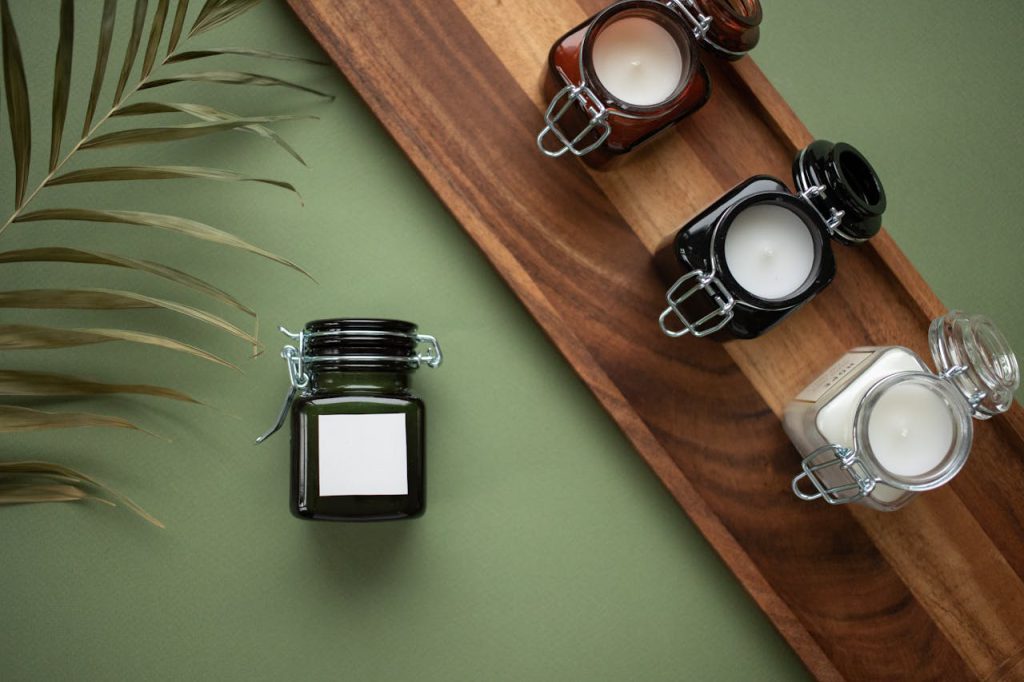 pexels-photo-6311803 Stylish arrangement of candles in glass jars on wooden tray against green background.