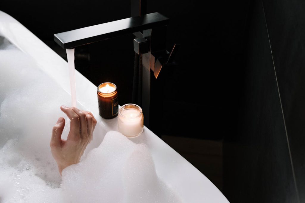 pexels-photo-8511481 A comforting bubble bath scene with lighted candles, showcasing a hand and running water for a tranquil atmosphere.
